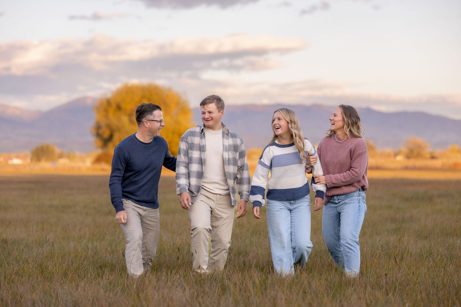 A group walks together through a golden wheat field at sunset while wearing casual clothing.