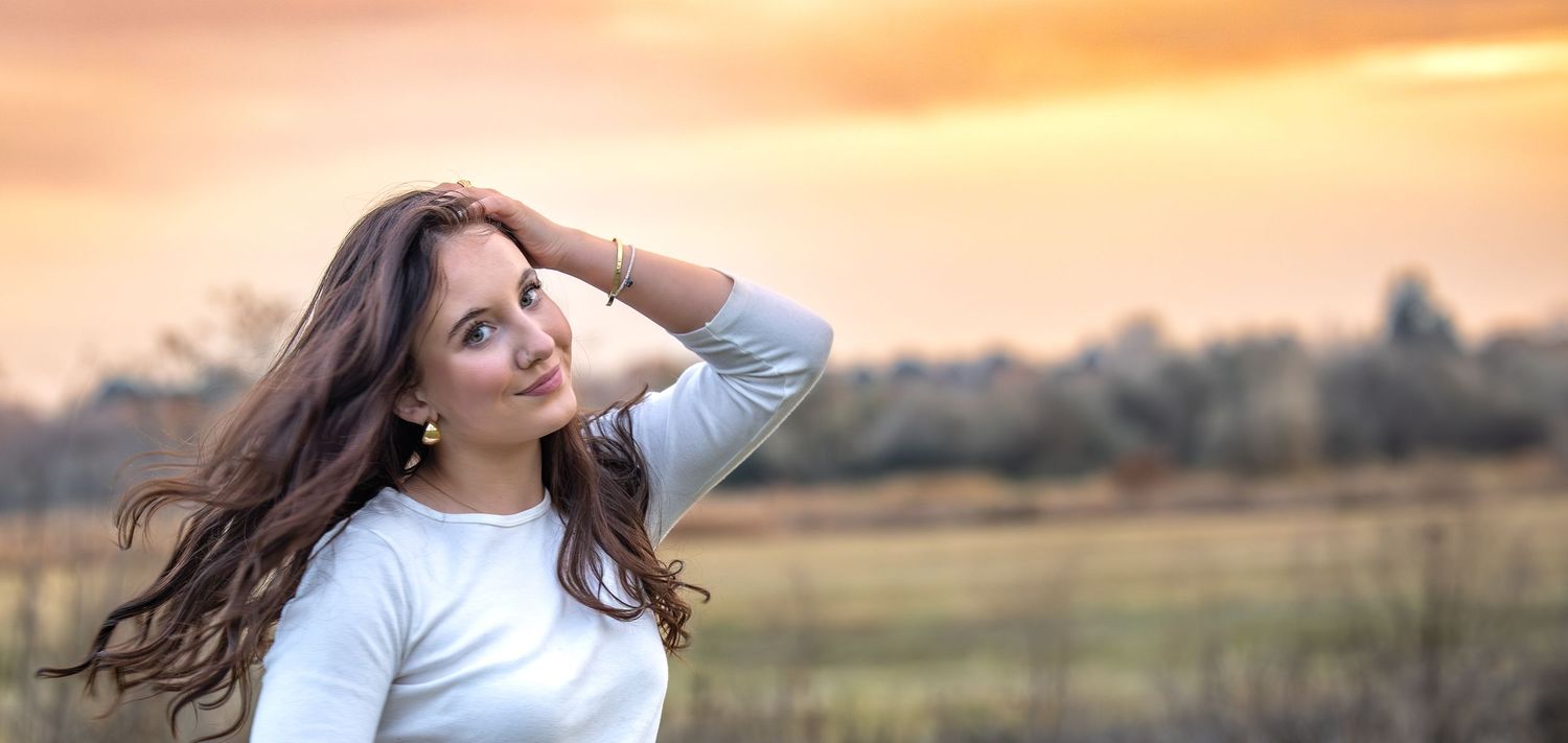 Person in white poses gracefully in a field at sunset with warm autumn colors.