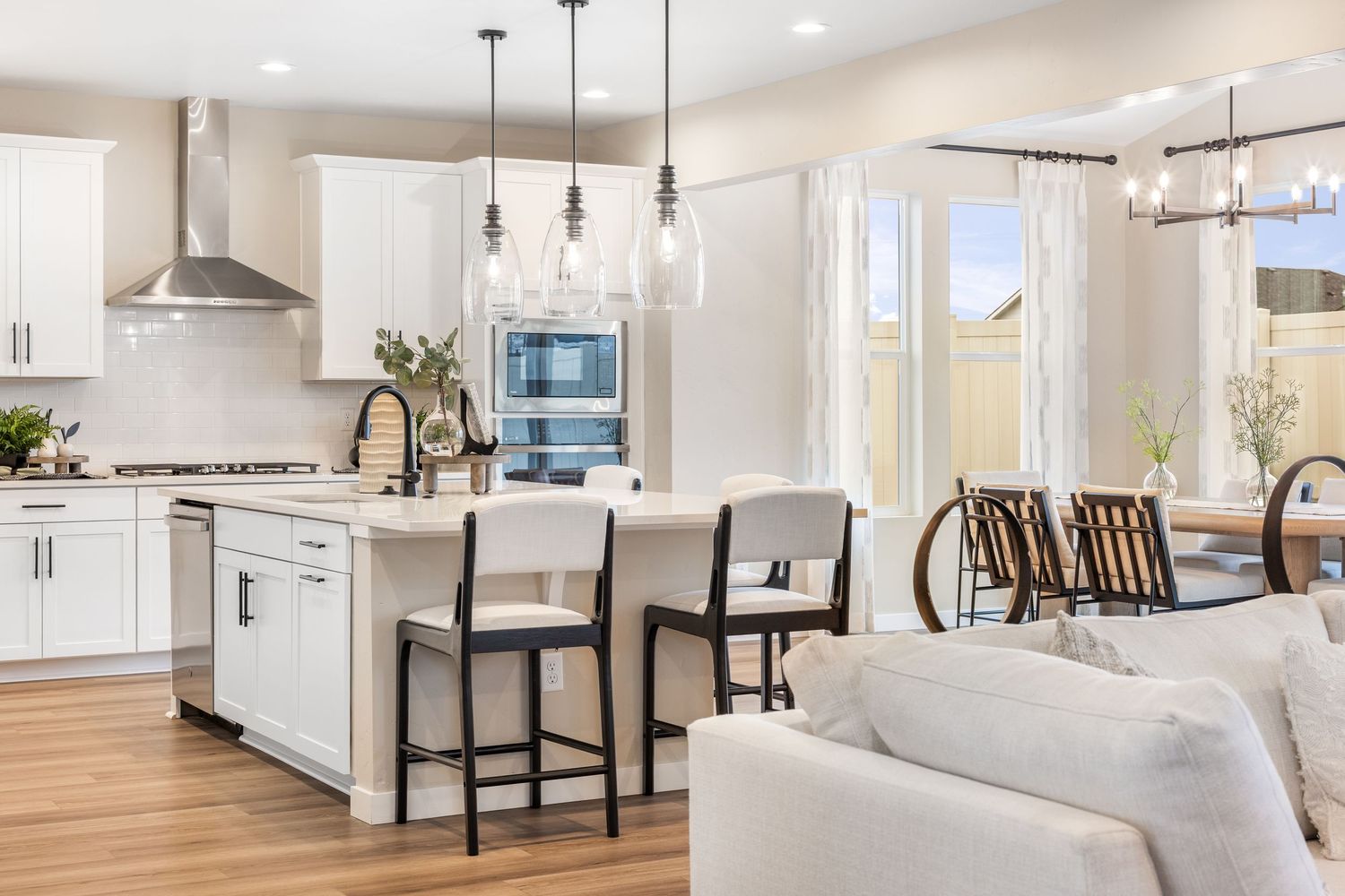 Modern open concept kitchen and living room with white cabinets, pendant lights, and hardwood floors in new construction home.