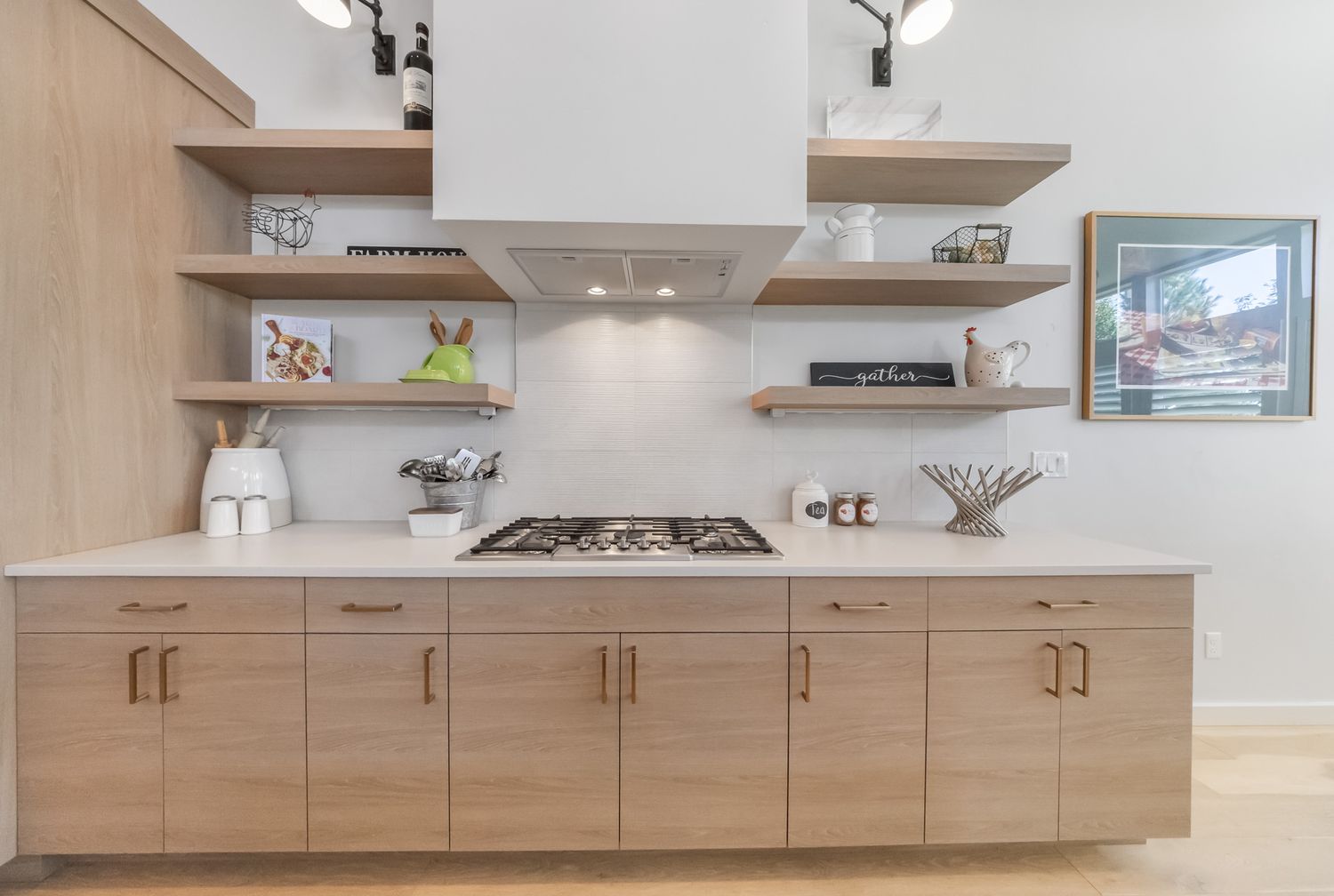 Modern kitchen design featuring floating wooden shelves and light wood cabinetry with white countertops and backsplash.