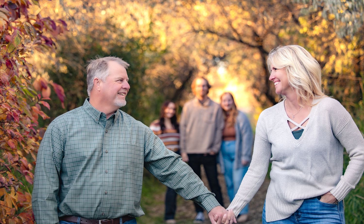 Family members laugh and embrace while posing for casual outdoor photos in autumn scenery.