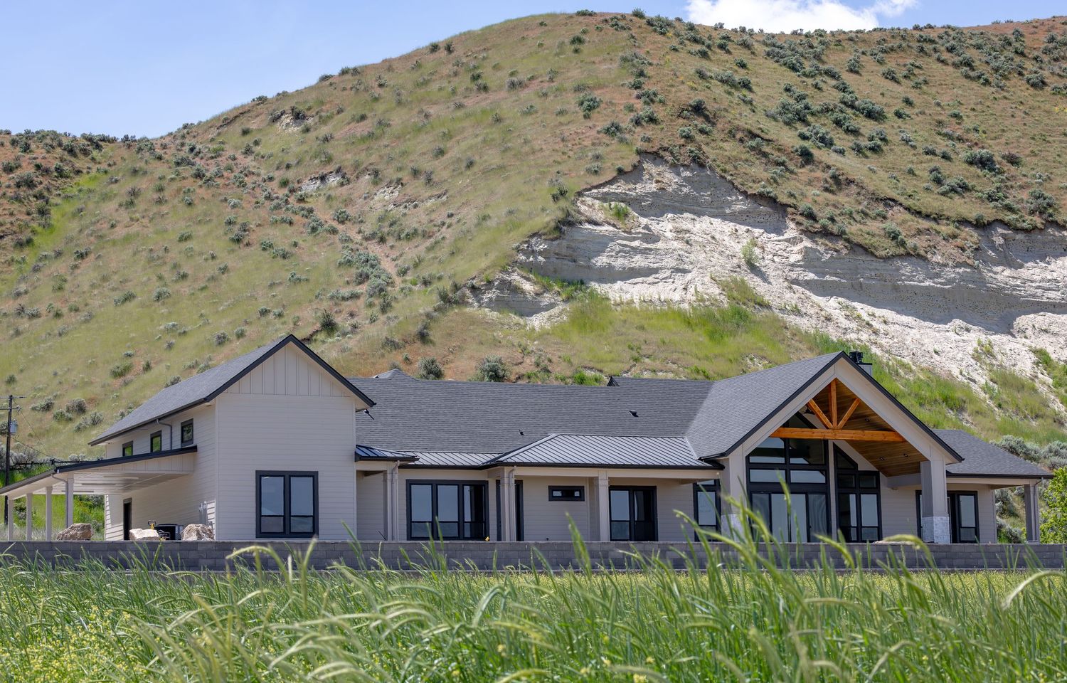 Modern ranch-style home nestled against a green hillside with rocky cliffs, surrounded by natural grasslands.