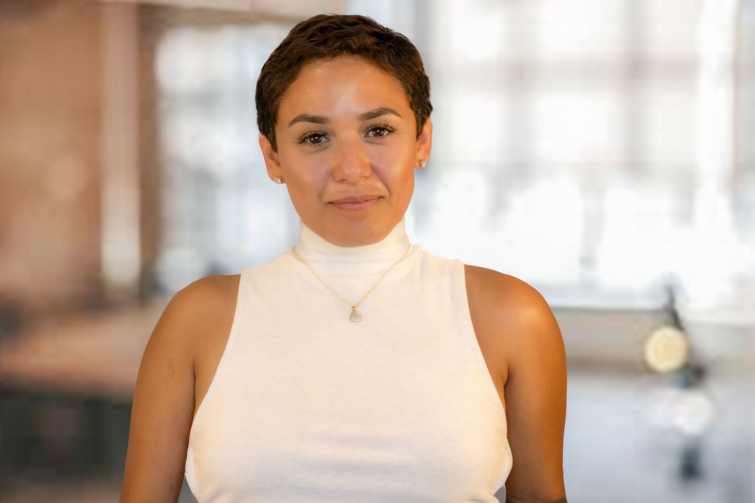 Person wearing white sleeveless top smiles in well-lit indoor setting with blurred background.