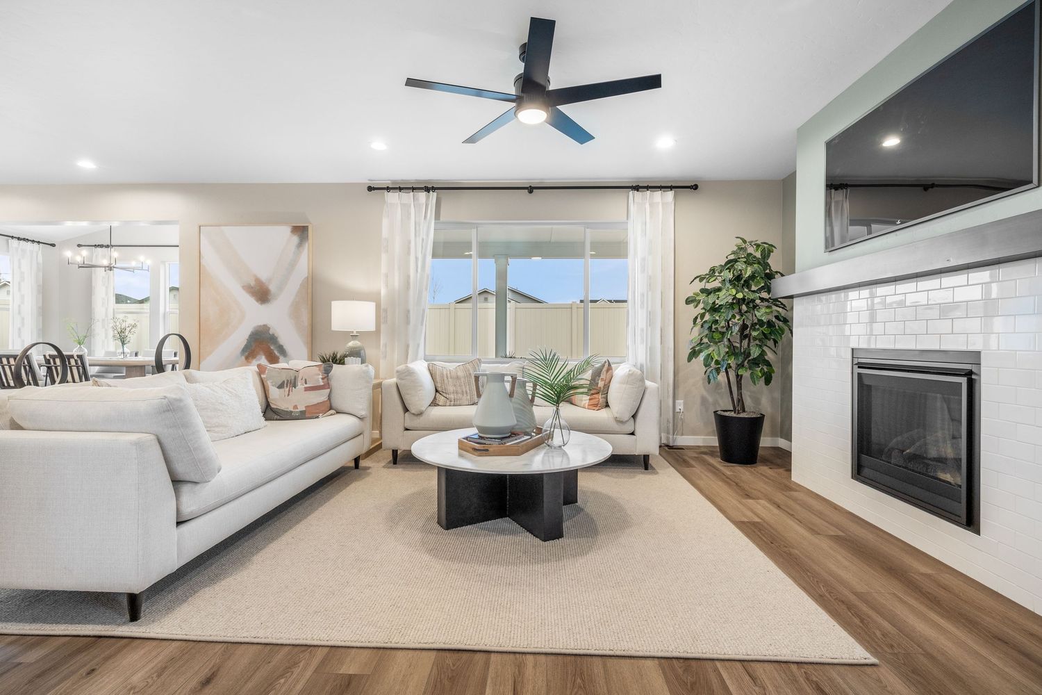 Contemporary living room with white sofa, ceiling fan, hardwood floors and large windows overlooking scenic views.