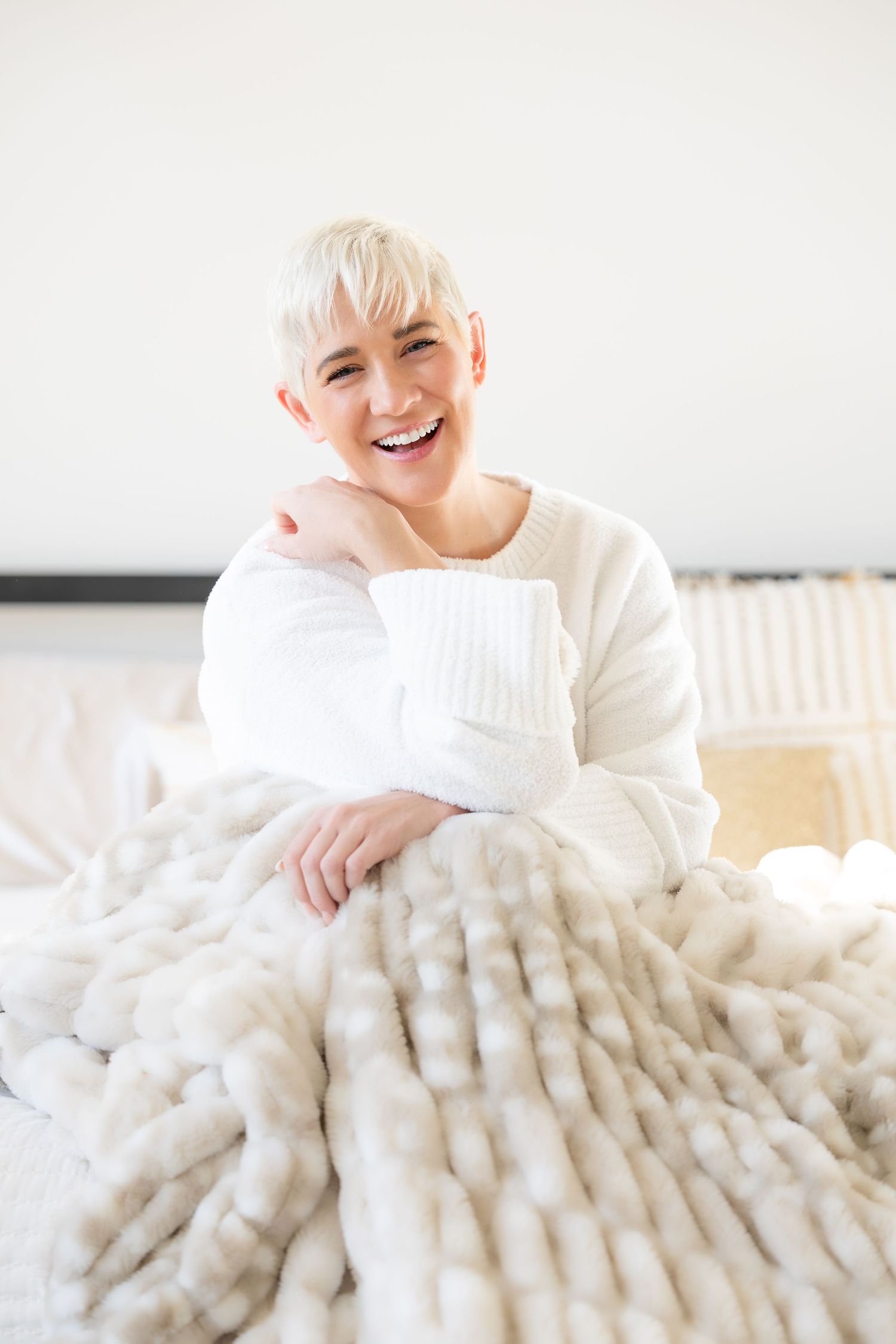 A series of photos showing someone wearing a white sweater relaxing on a plush chunky knit blanket while smiling.