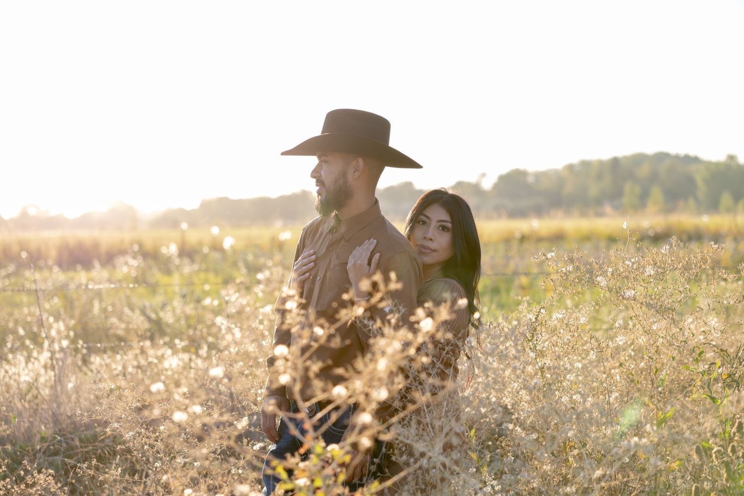 Couple in cowboy hats share romantic moments in a golden sunlit field during sunset.