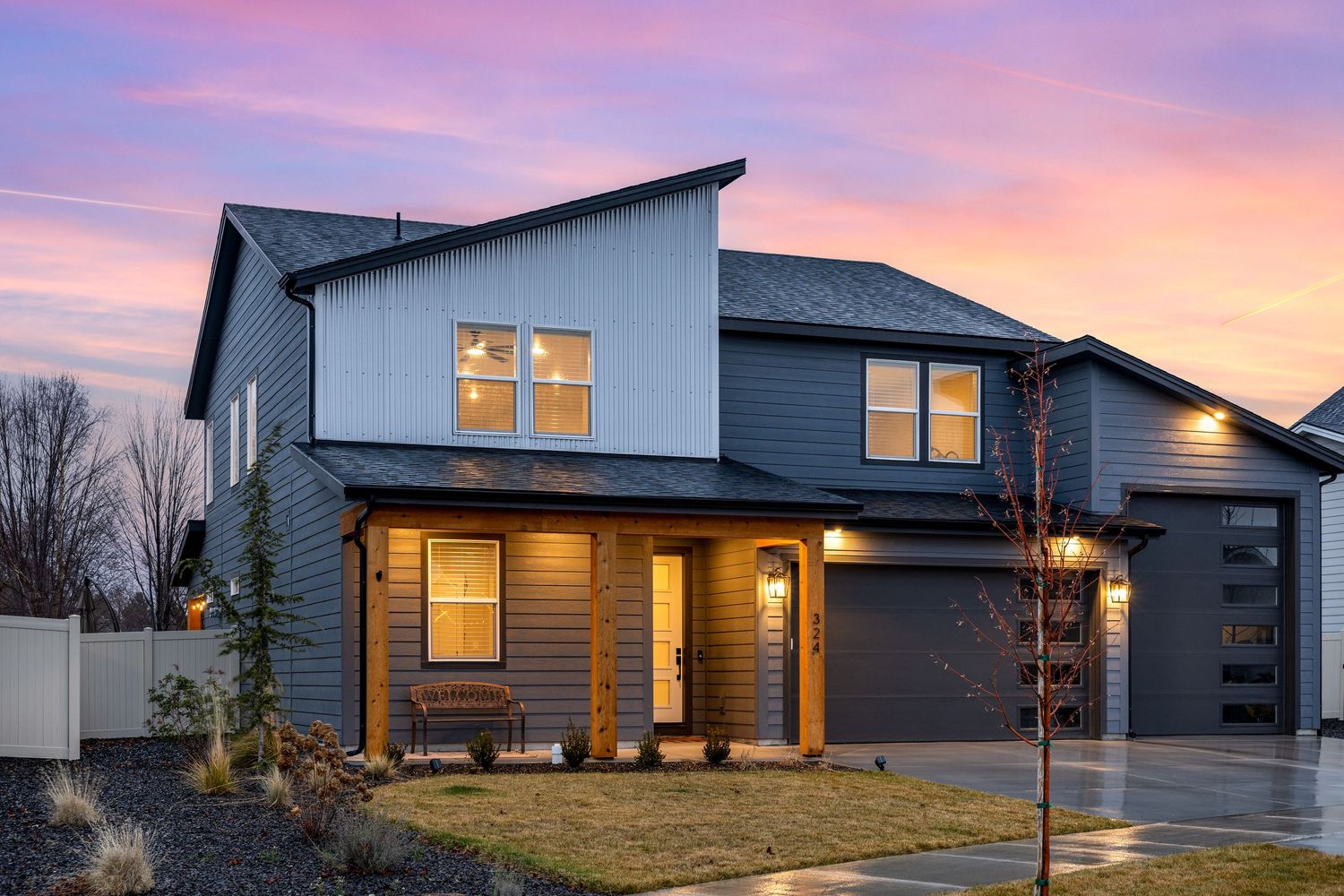 Modern residential homes illuminated at sunset showcase warm glowing windows against a vibrant purple and orange sky.