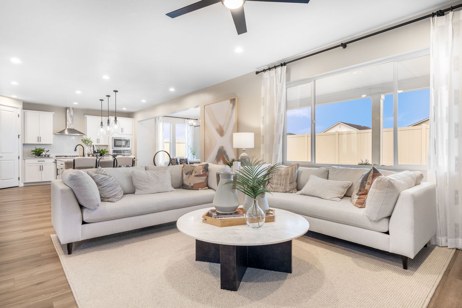 Modern open concept living room features a ceiling fan, light hardwood floors, and panoramic windows with city views.