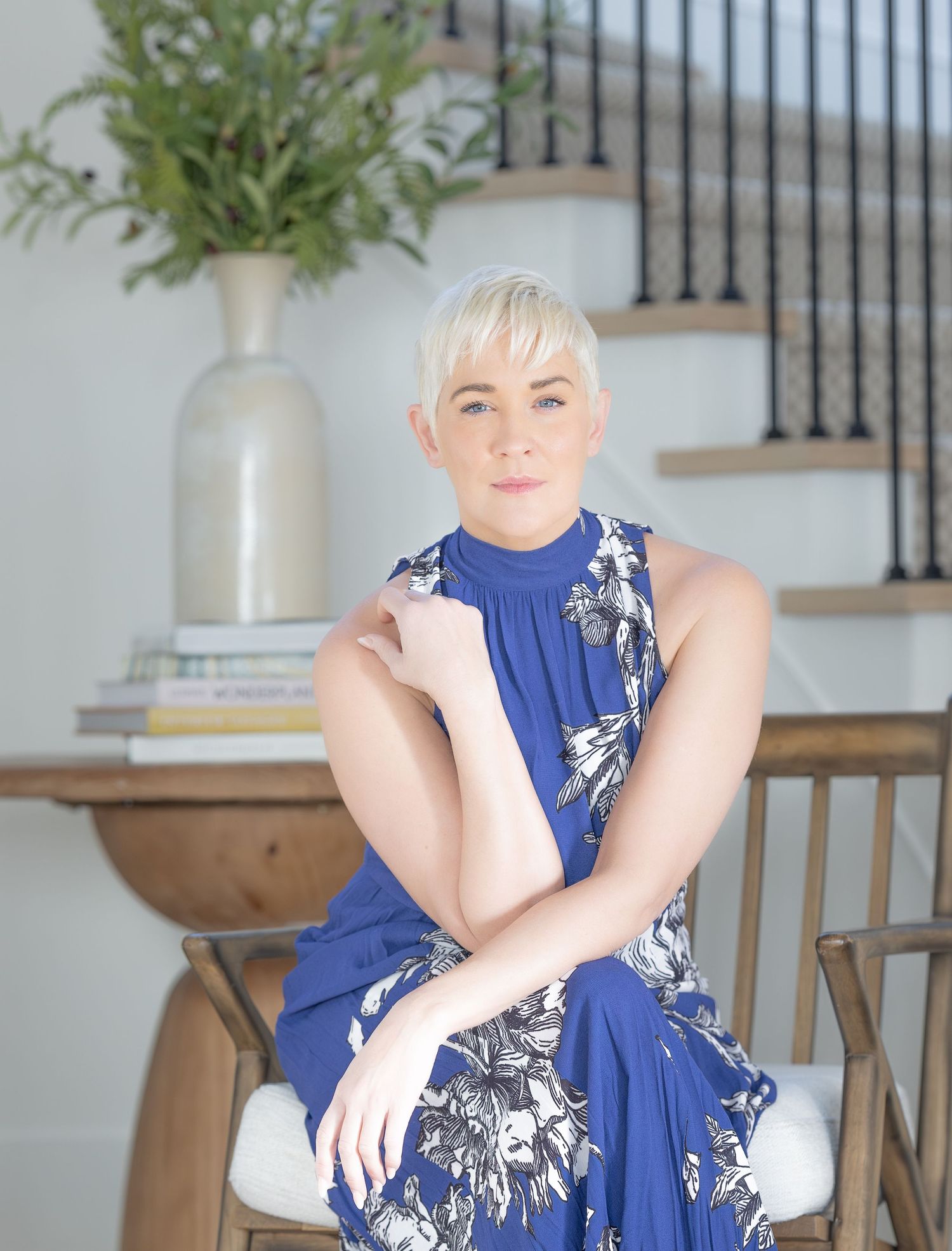 Person in a navy blue floral dress poses in a series of casual shots against a light interior background with stairs.
