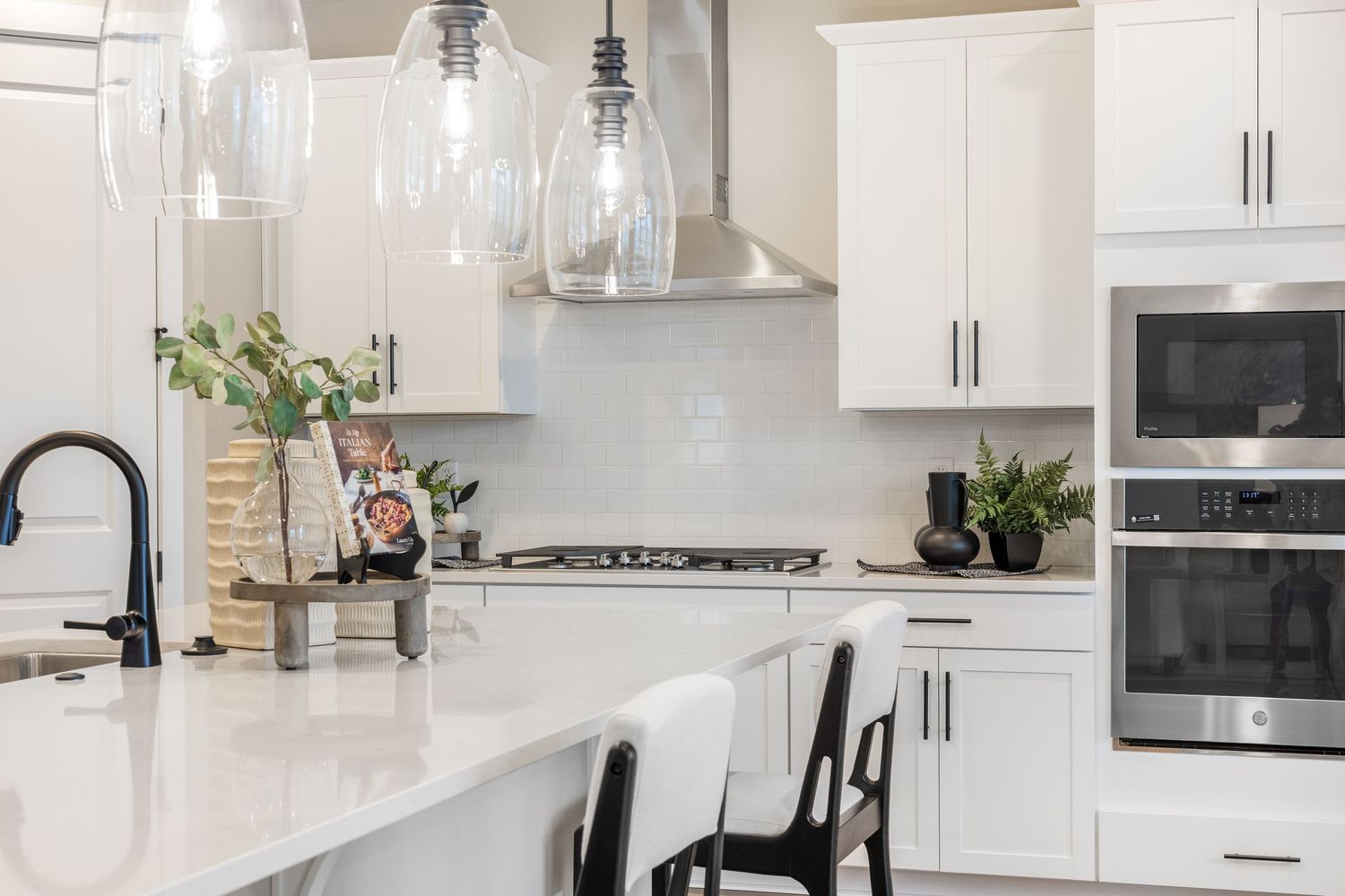Modern white kitchen with quartz countertops, glass pendant lights, and black bar stools at a large center island.