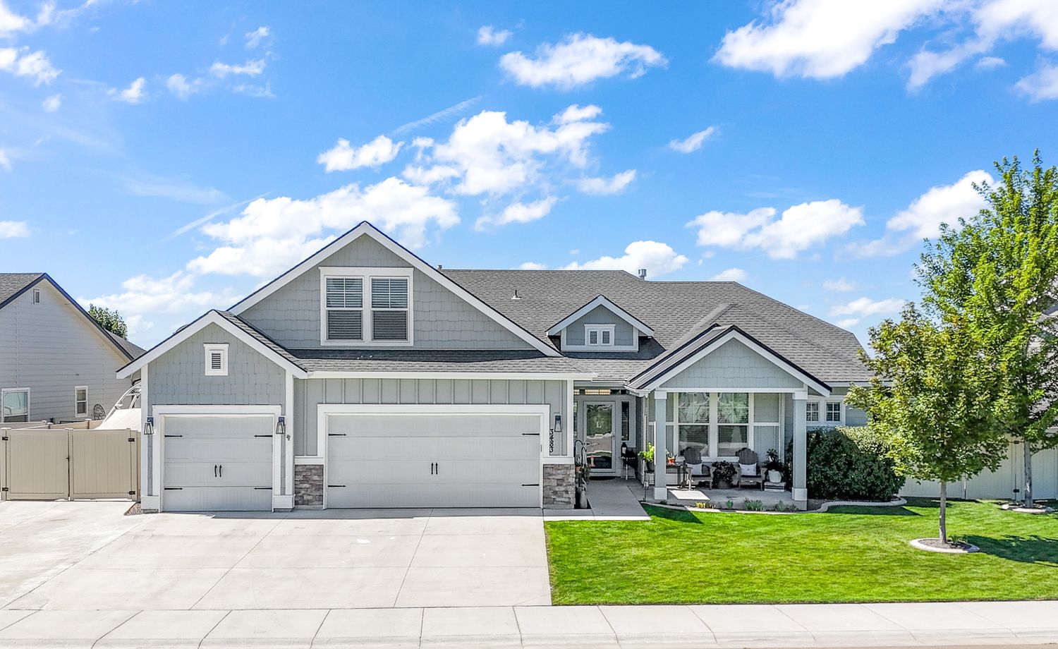 Modern gray and white ranch-style home with three-car garage and manicured lawn under blue sky with puffy clouds.