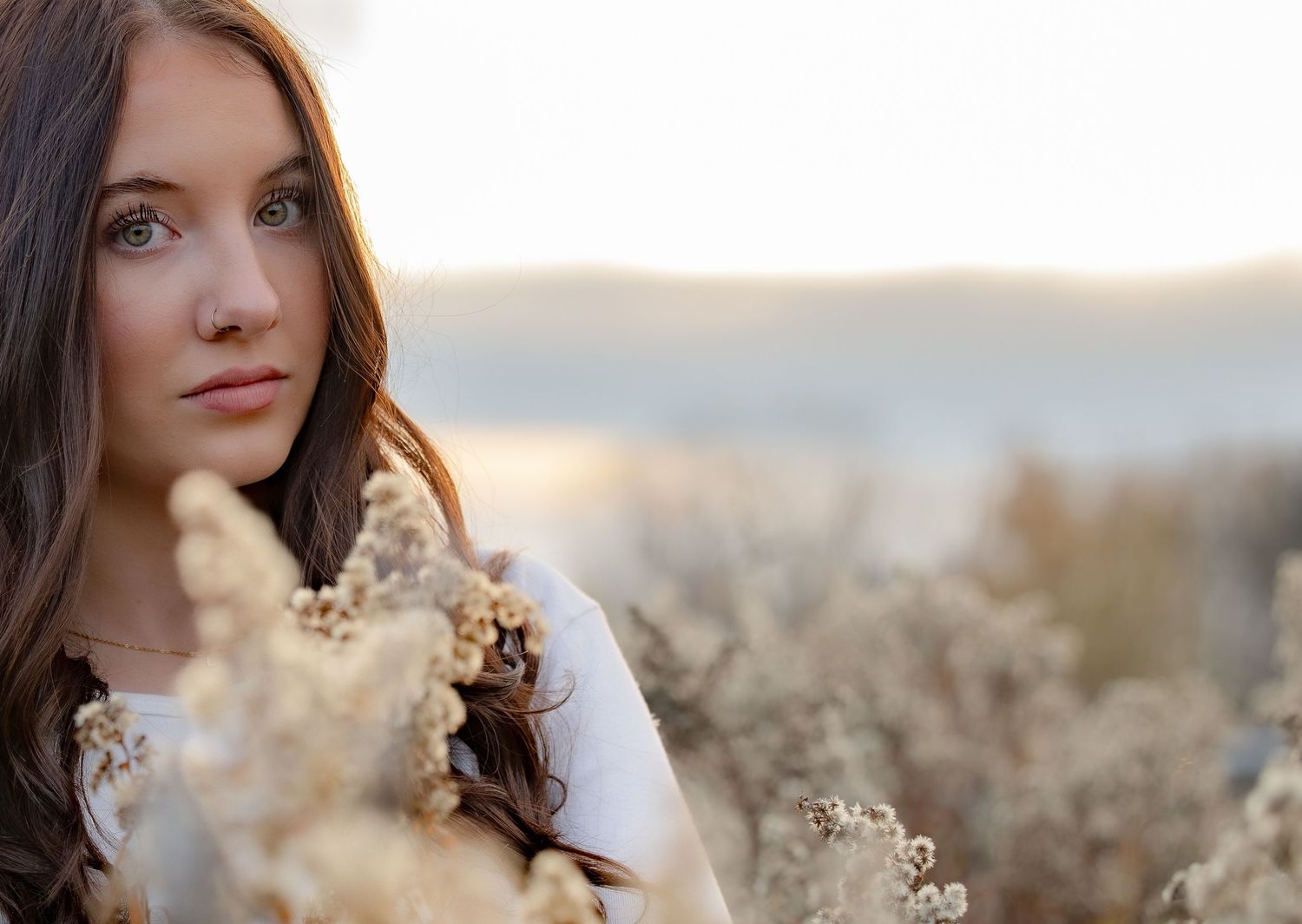 Person in a white sweater poses thoughtfully among dried plants during golden hour.