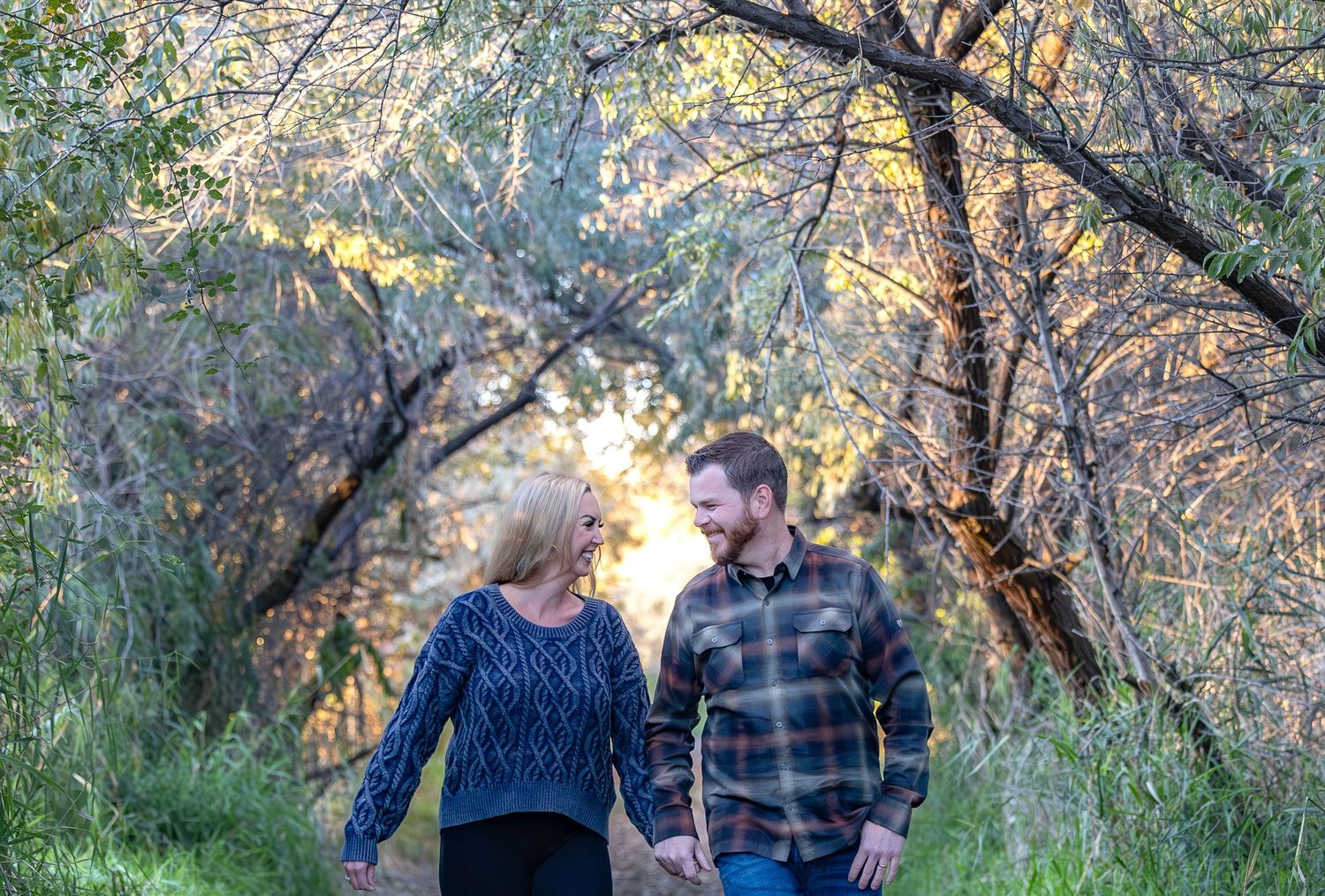 A couple walking together on a nature trail during sunset with golden light filtering through autumn trees.