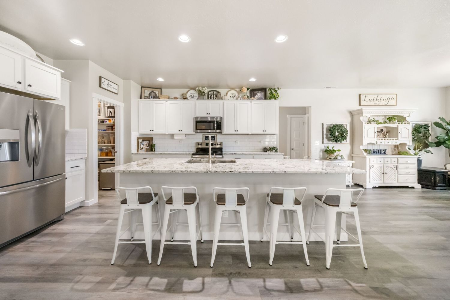 Modern white kitchen design with white counter stools, open shelving, and light hardwood flooring.
