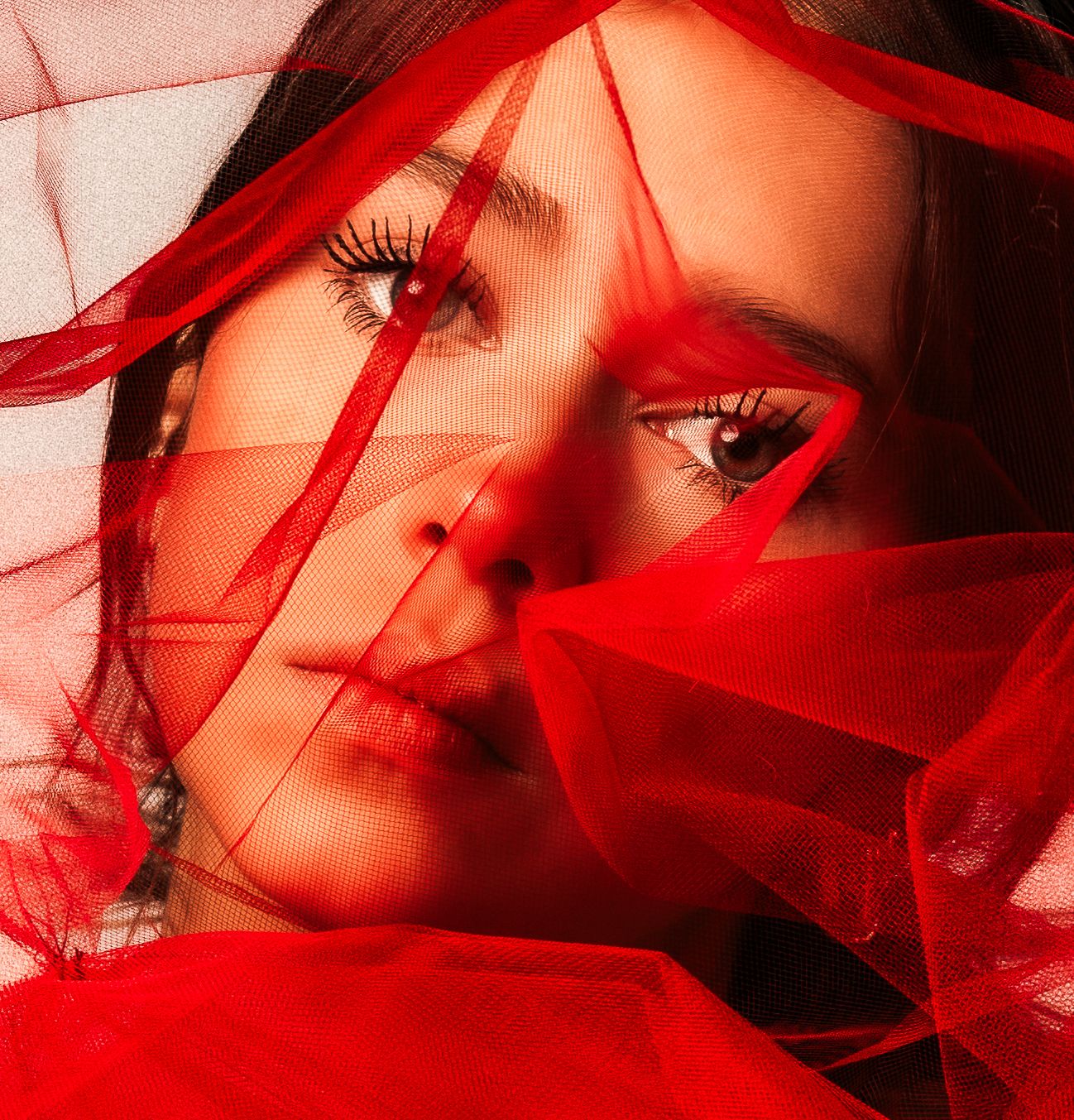 Artistic portrait in red lighting with dramatic shadows and wind-blown hair creating a moody atmosphere.