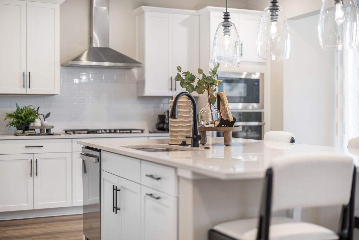 Modern white kitchen with quartz countertops, stainless steel appliances, and pendant lighting over a large center island.