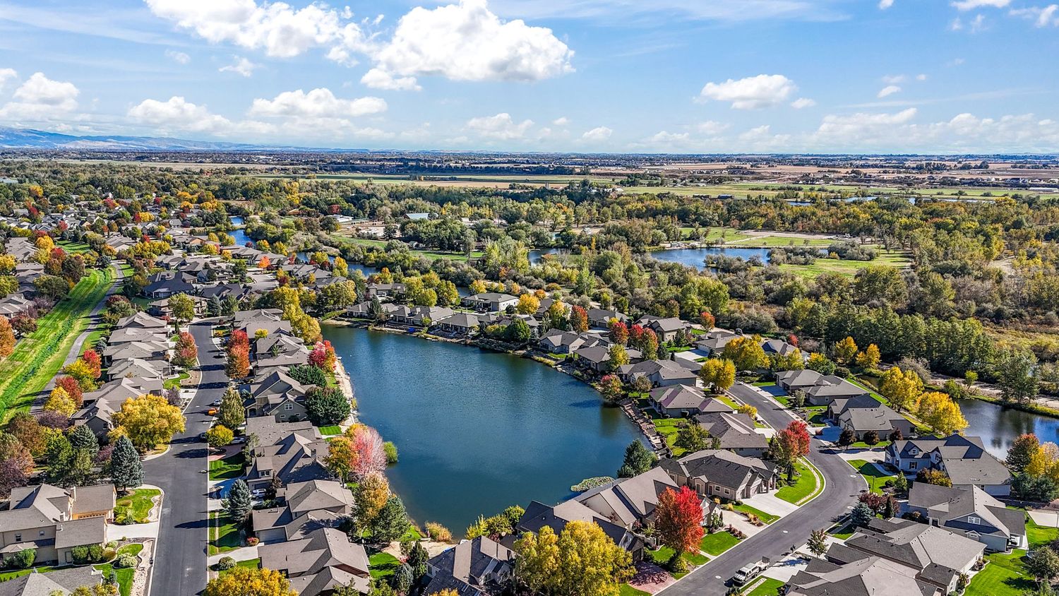 Sweeping aerial panorama showing residential neighborhoods surrounding a lake with autumn foliage and clear skies.