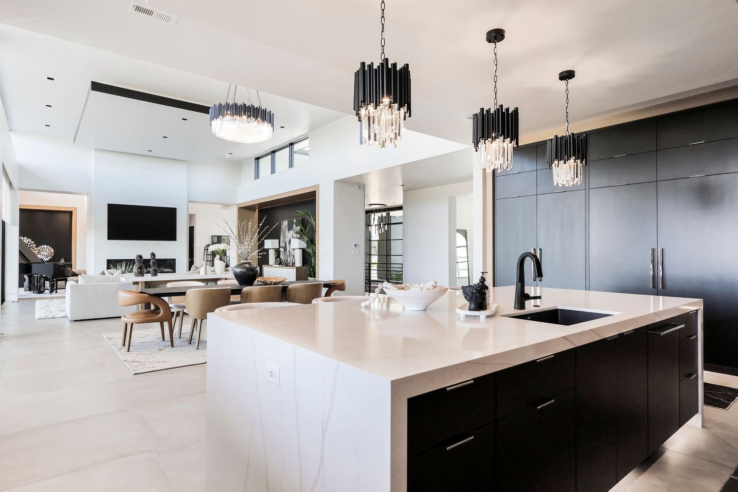 Modern luxury kitchen and living space with black and white design featuring contemporary chandeliers and sleek island.