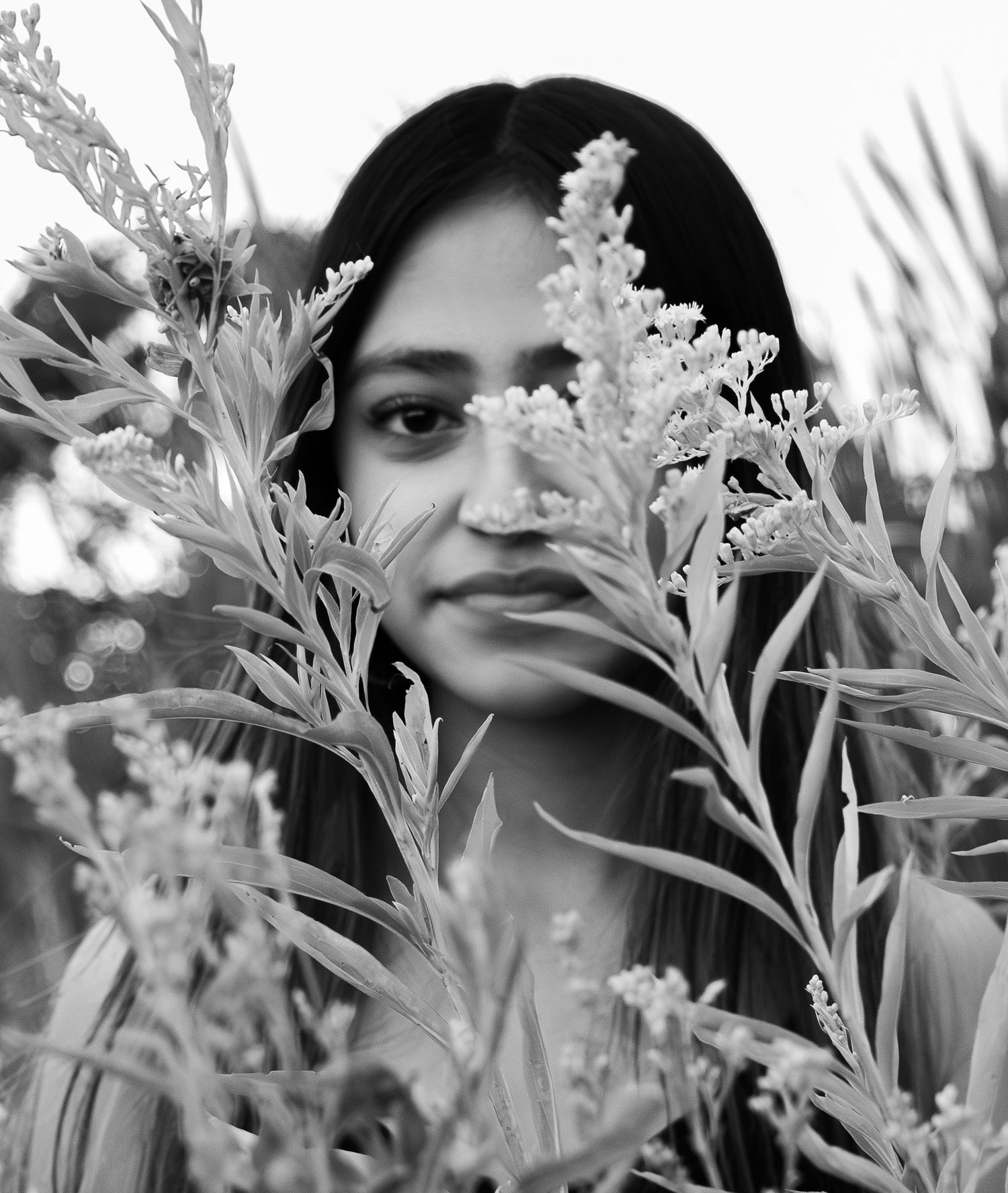 Black and white portrait photograph with delicate white flowers and foliage in the foreground creating a dreamy effect.