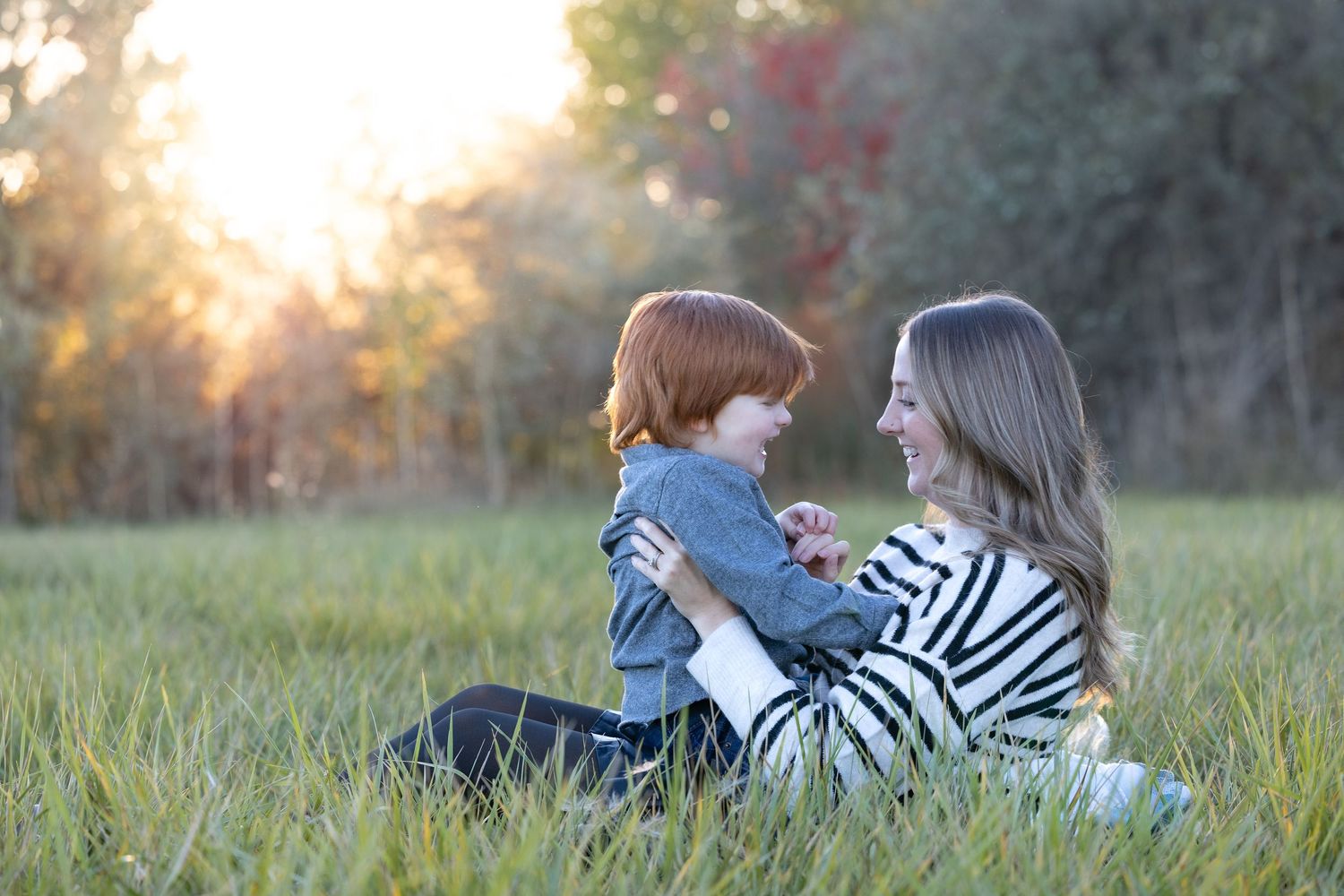 A tender moment between parent and child sitting together in a sunlit grassy field at golden hour.