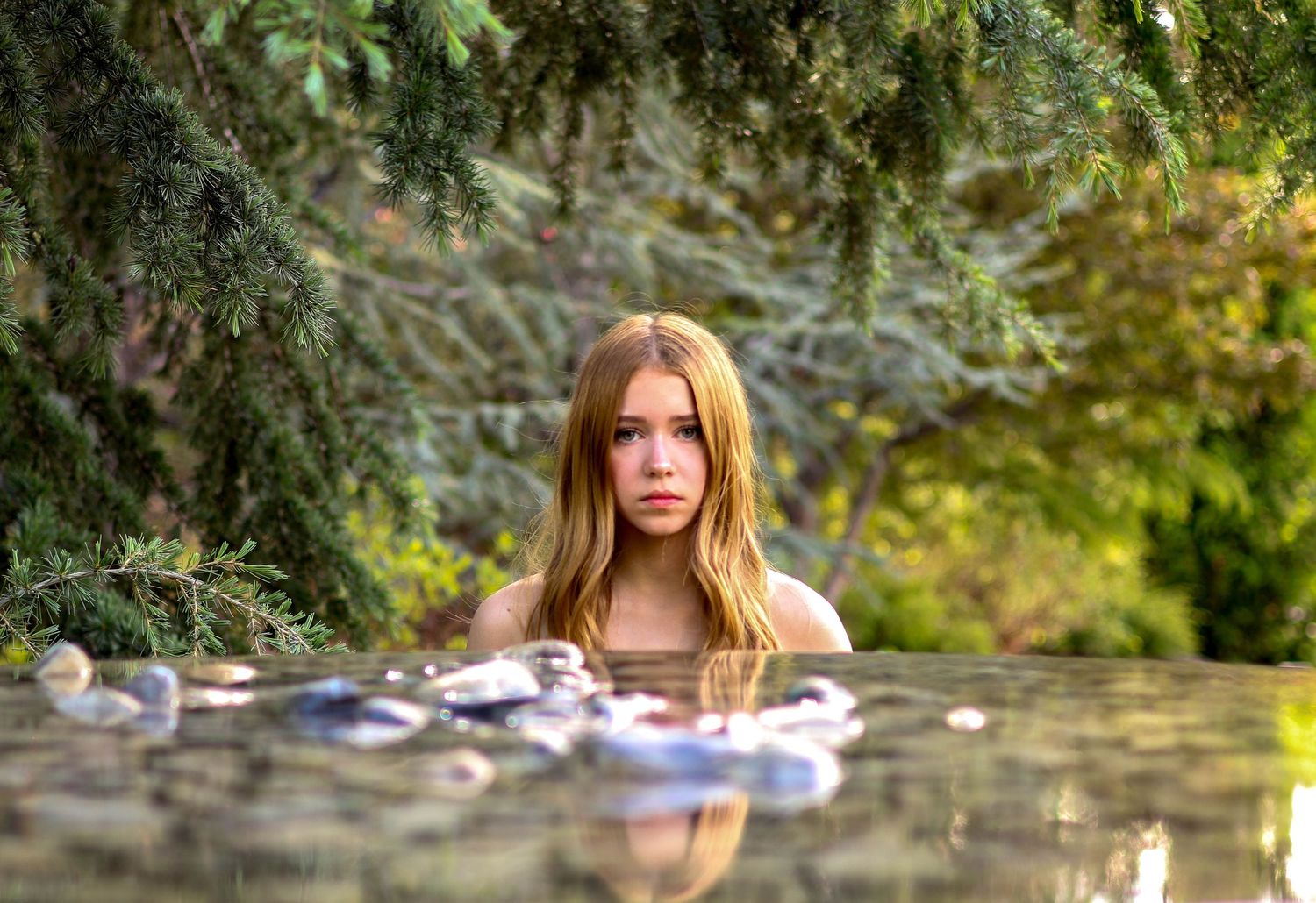 Person floating in reflective water surrounded by lush garden foliage.