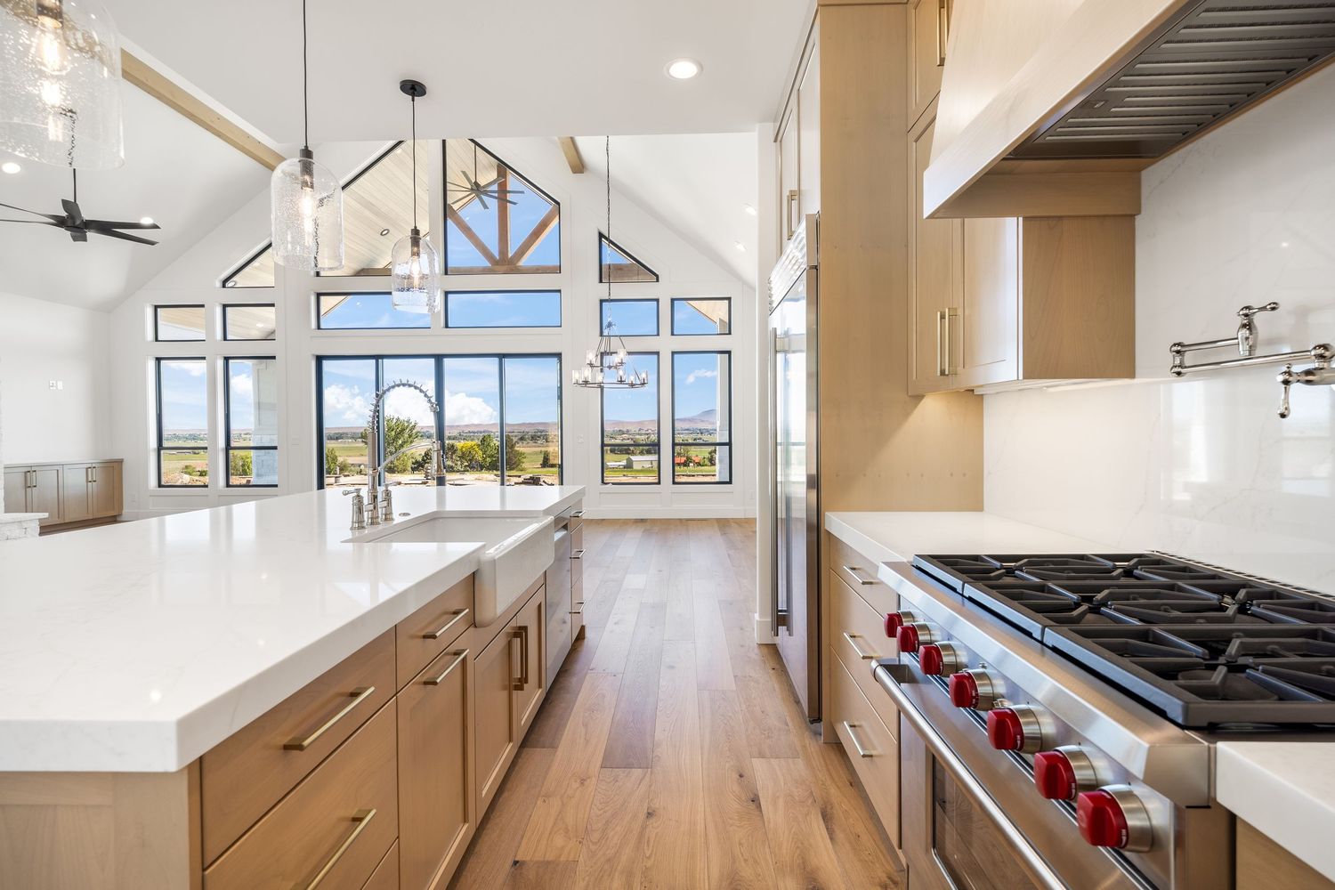 Modern kitchen with vaulted ceilings, large windows, white countertops, wood cabinets, and a professional stainless steel range.