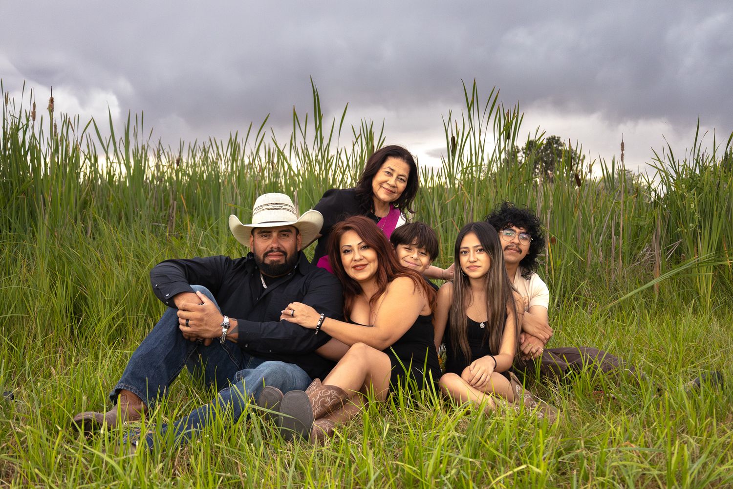 A group relaxes together in a tall grass field on a cloudy day.