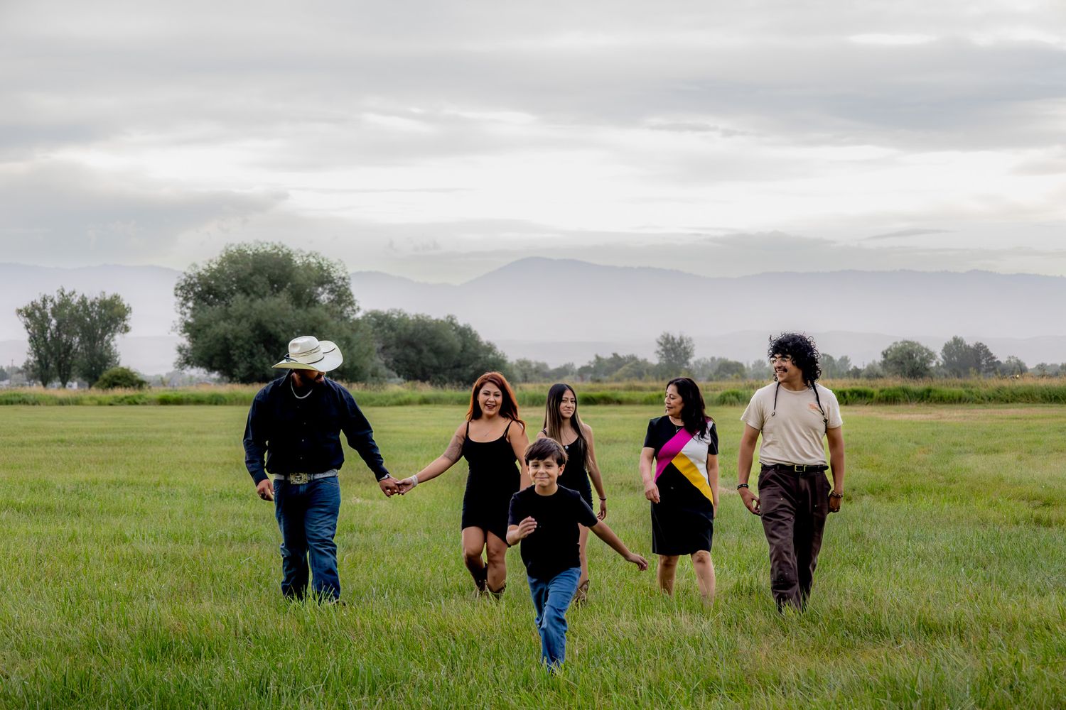 A group of people walk together across a vast green meadow under an overcast sky on a summer day.