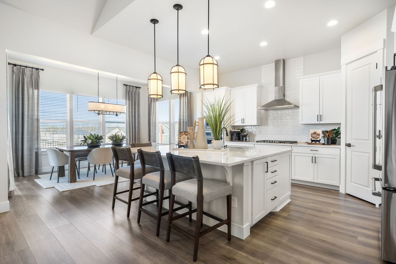 Modern white kitchen with pendant lights, hardwood floors, and stainless steel appliances showcases an open concept design.