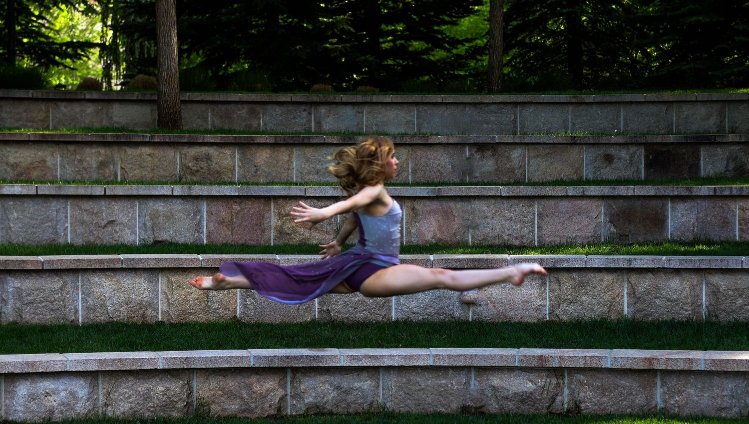 Dynamic dance pose showing a split leap on outdoor stone steps.