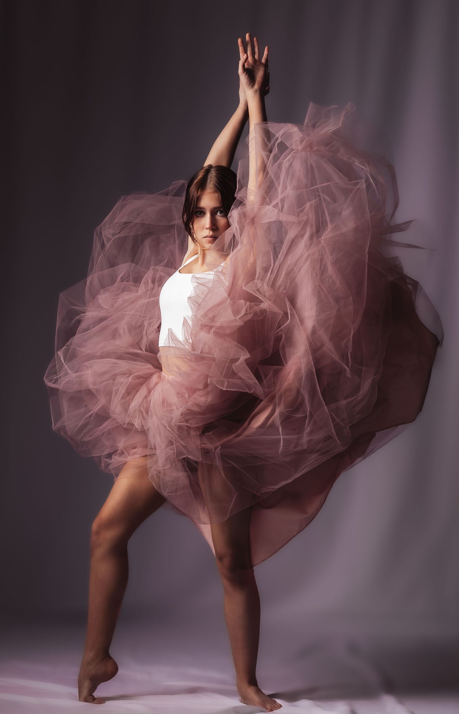 Dancer in pink tulle tutu skirt performs dynamic movement sequence against dark studio backdrop.