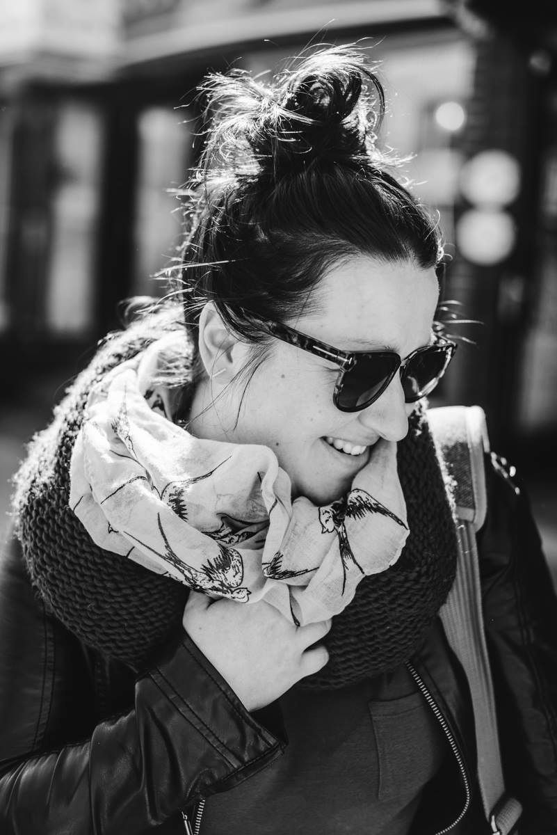 Black and white portrait of Caroline Lessard Photographe with sunglasses and a cozy scarf, smiling with hair in a messy bun.