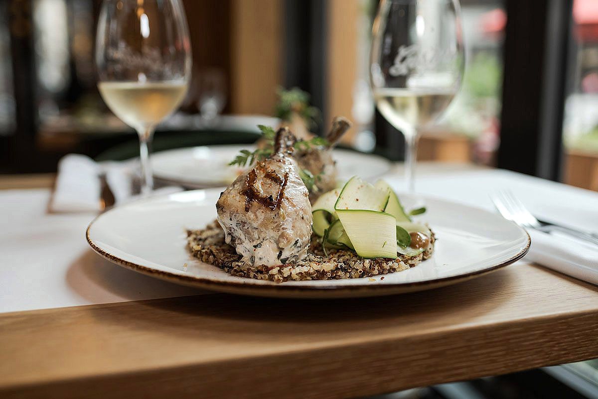 Elegant plated dish with meat and garnishes served alongside wine glasses on wooden restaurant table.