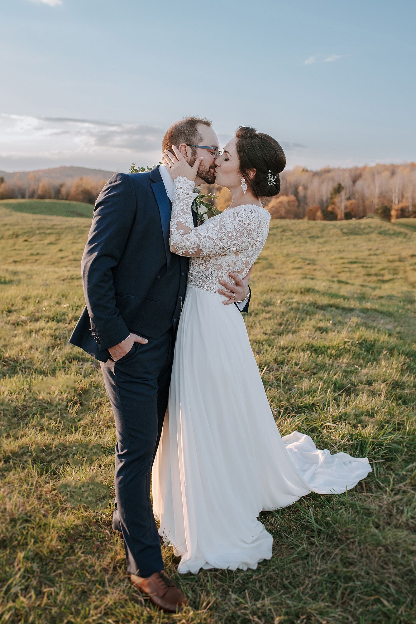 A romantic wedding couple embraces in a scenic field with rolling hills and autumn trees in the background. Auberge West Brome.