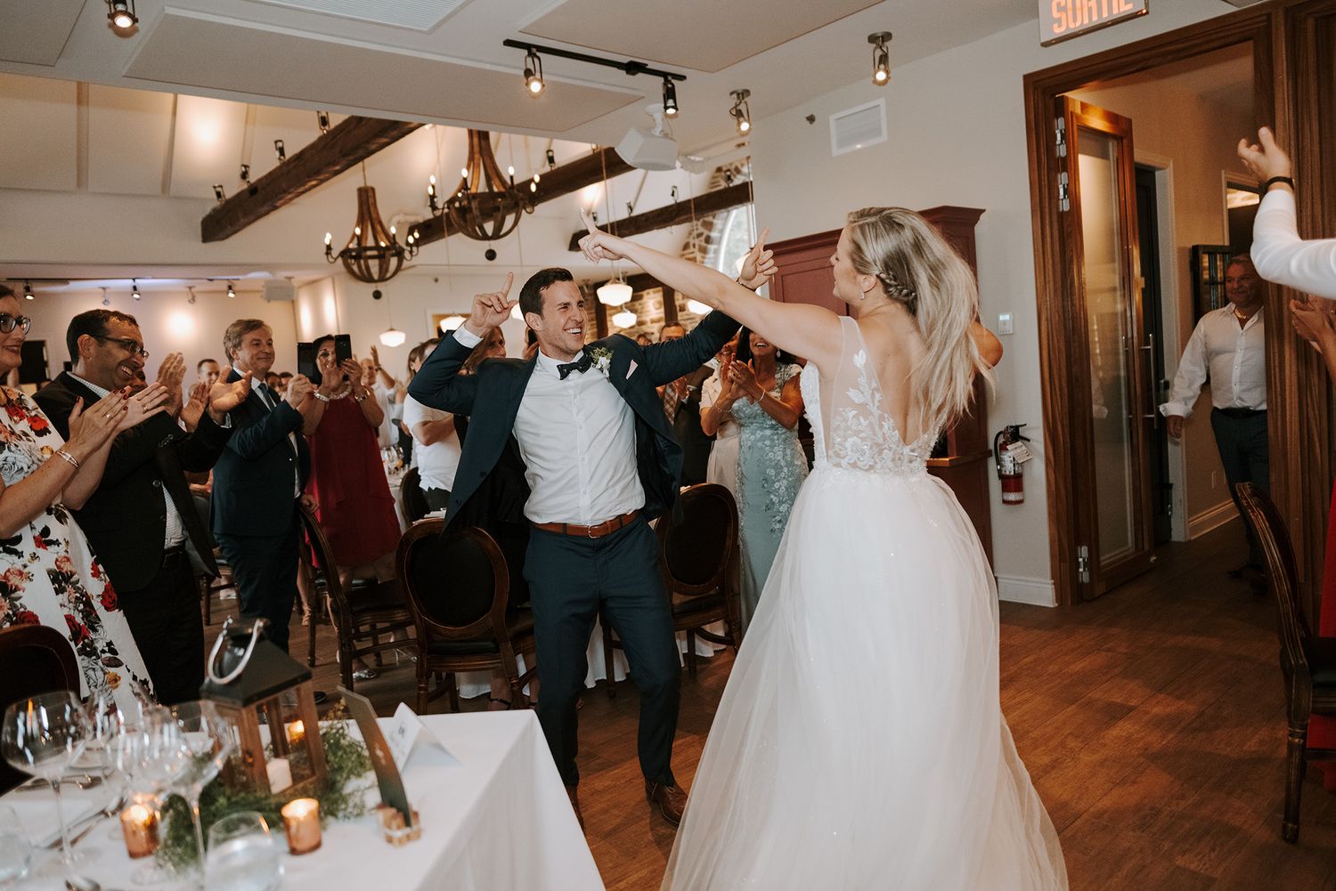 Wedding party celebrates with joyful dancing in an indoor reception venue with hardwood floors and track lighting. Vignoble Le Ruisseau.