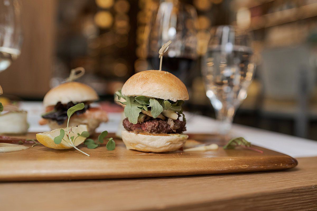 Gourmet burger with melted cheese and microgreens served on a wooden board in a restaurant setting.