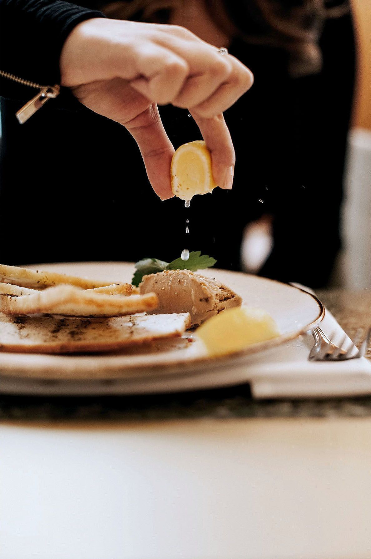 Hand squeezing lemon over a plated dish with garnish in an elegant restaurant setting captured by Caroline Lessard photographe Montréal.