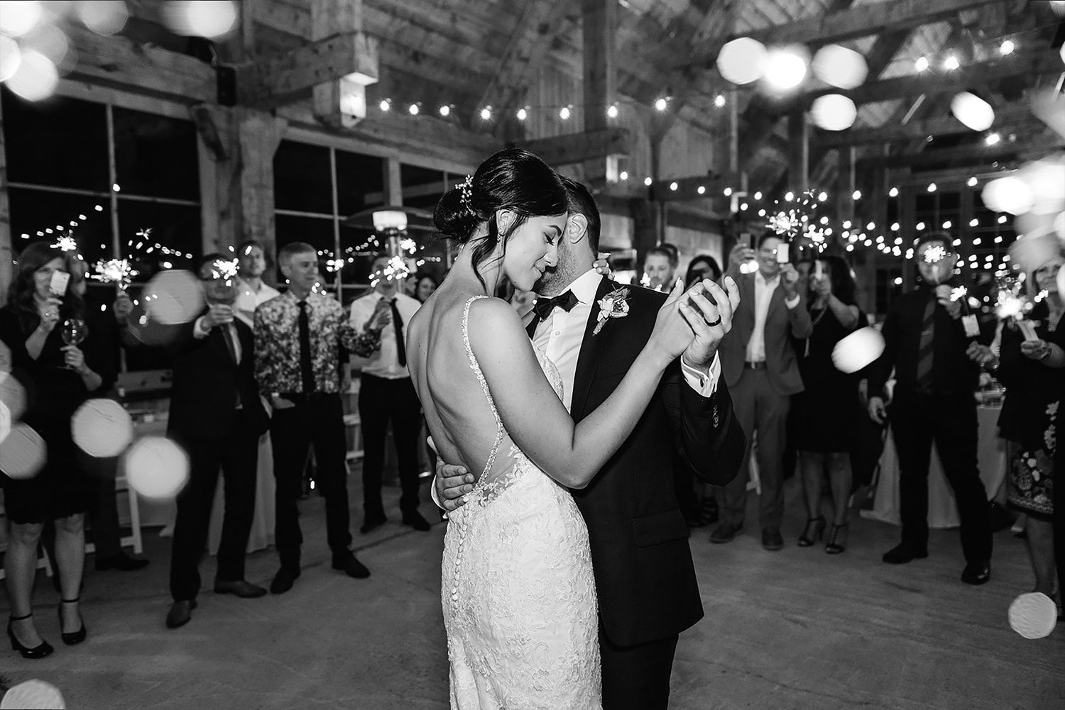 A bride and groom share their first dance beneath twinkling lights at an indoor wedding reception venue. Pont couvert La Conception.