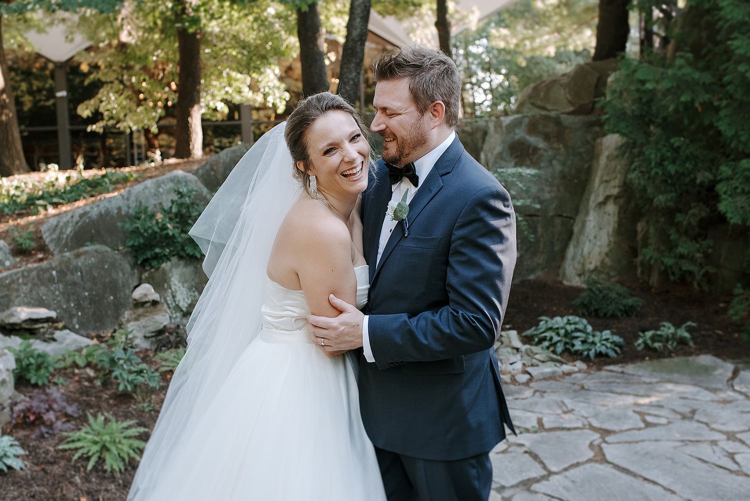 A couple shares a joyful moment together on their wedding day along a stone pathway surrounded by lush greenery. La Toundra.
