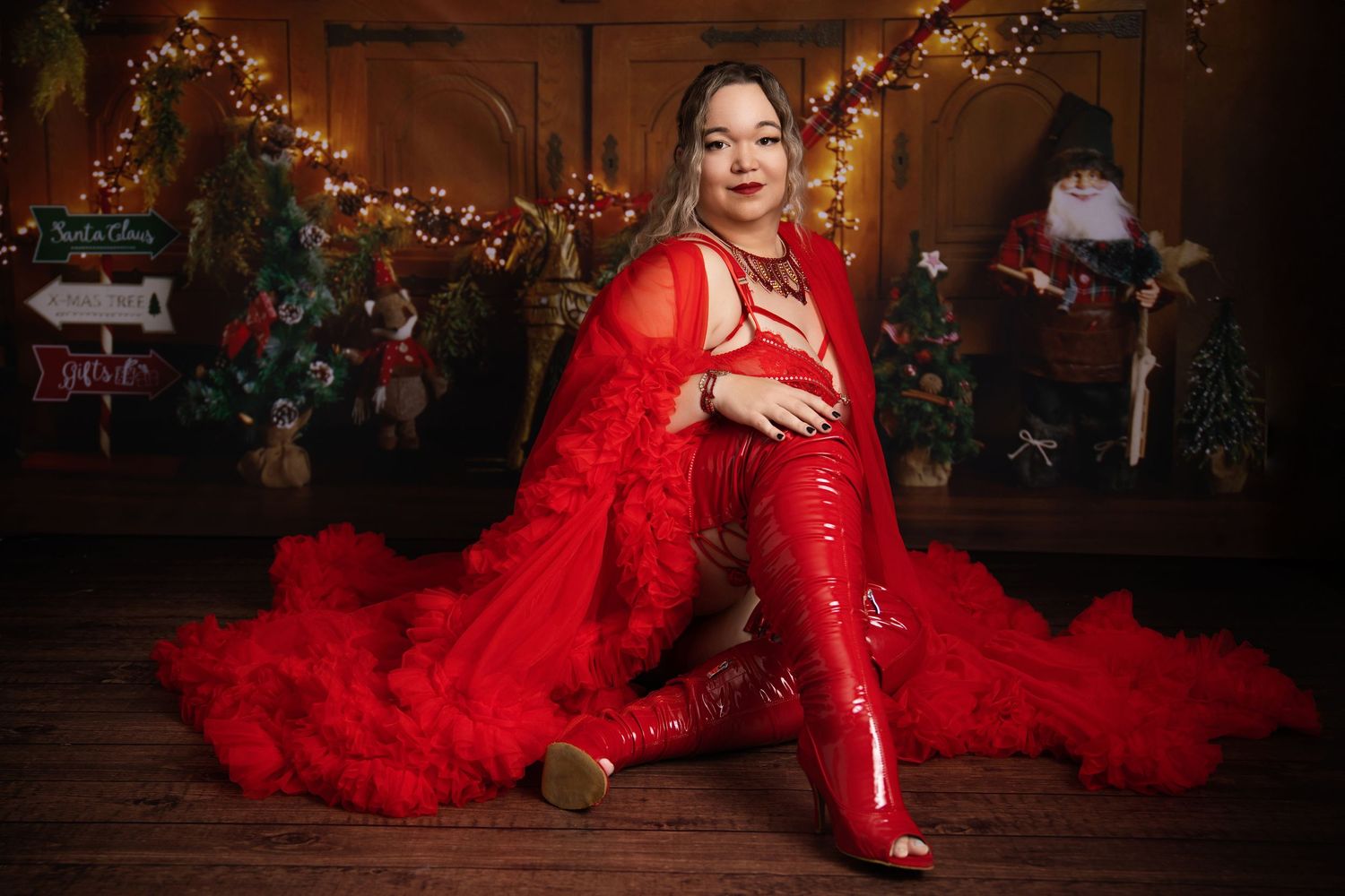 A person in a glamorous red tulle gown poses against a rustic wooden backdrop with Christmas decorations.