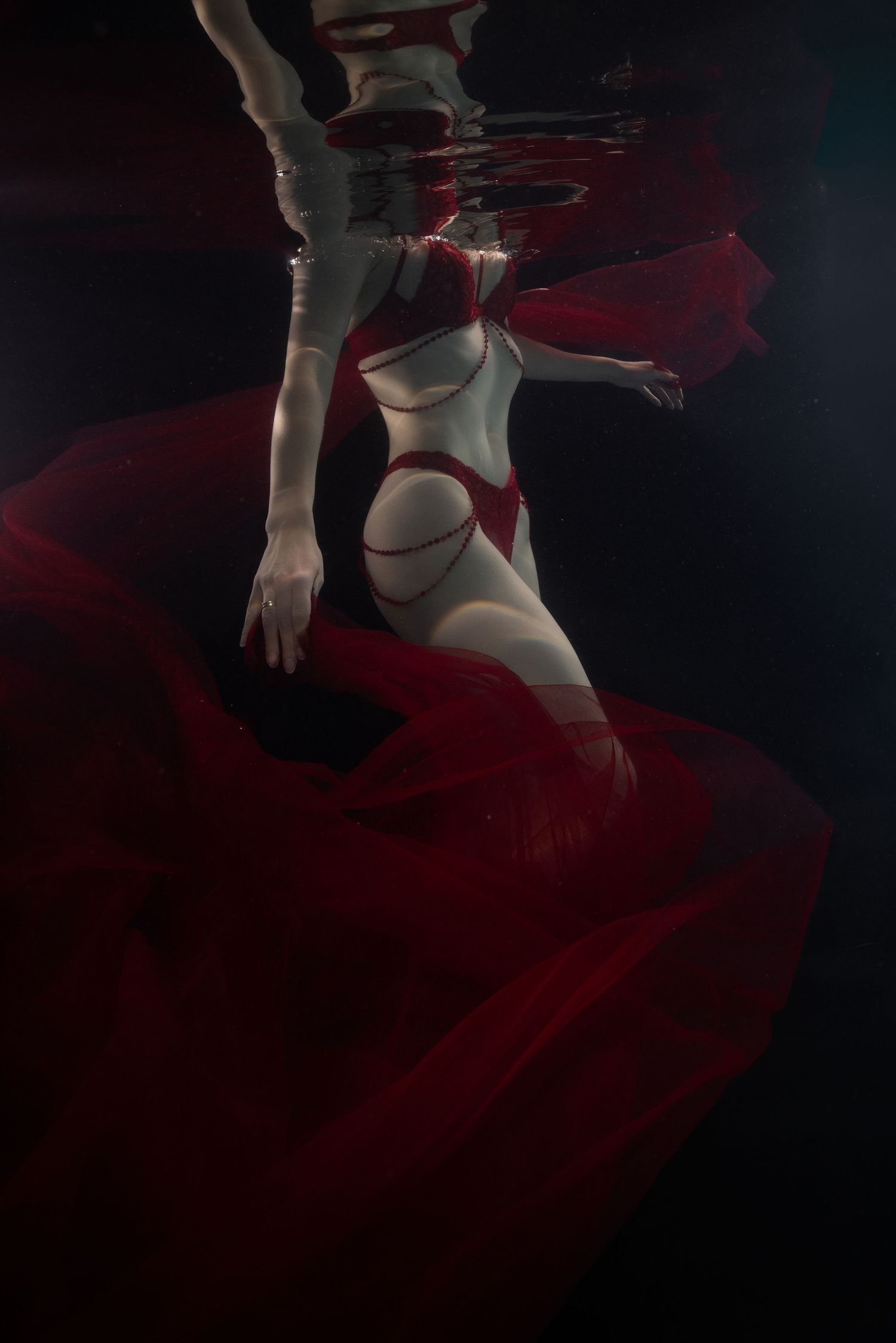 Underwater photo of a woman in a white and red swimsuit with flowing red fabric billowing around her in dark water.