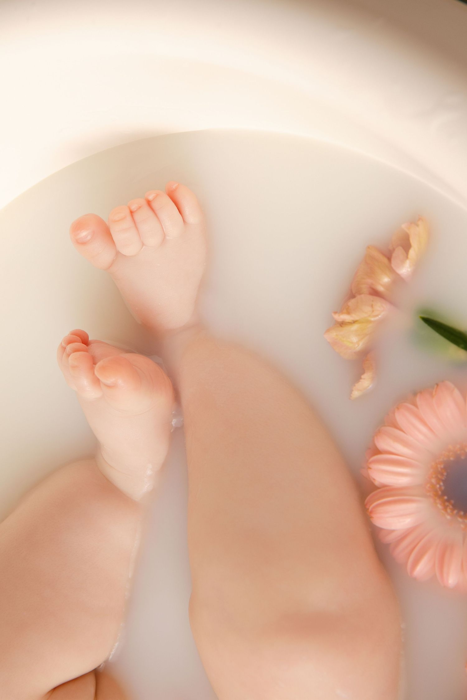 Tiny baby feet rest beside delicate pink flowers on a soft white surface creating a gentle newborn portrait.