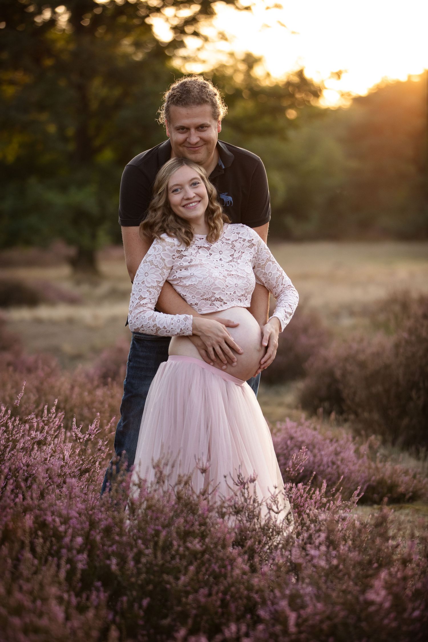 A couple embraces in a beautiful sunlit field of purple heather during golden hour.