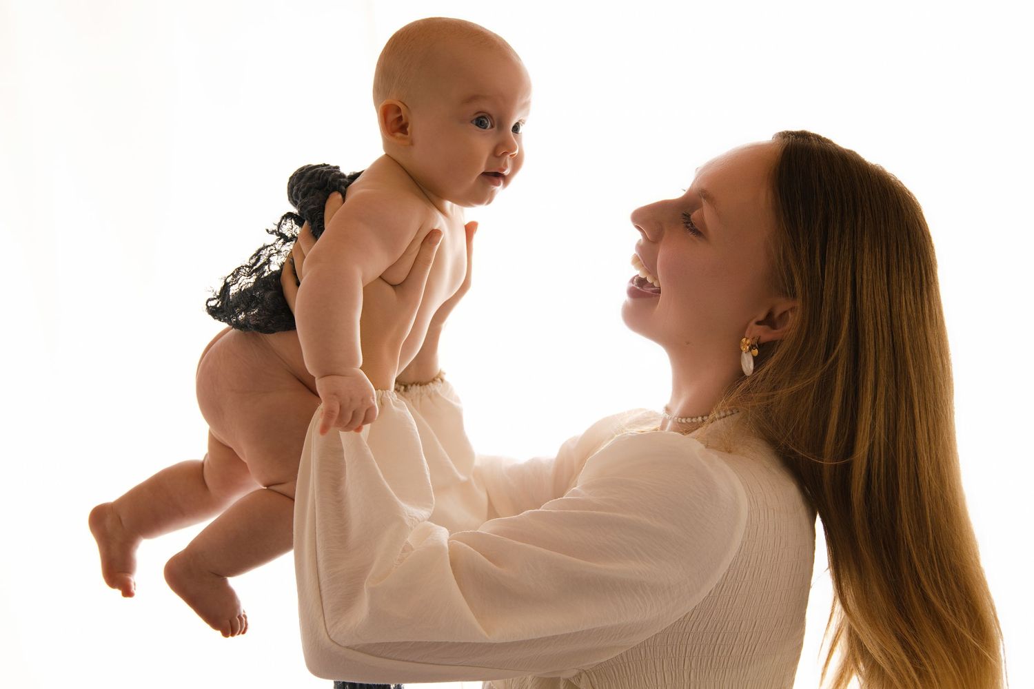A joyful interaction between parent and baby wearing a black and white patterned outfit against a white backdrop.