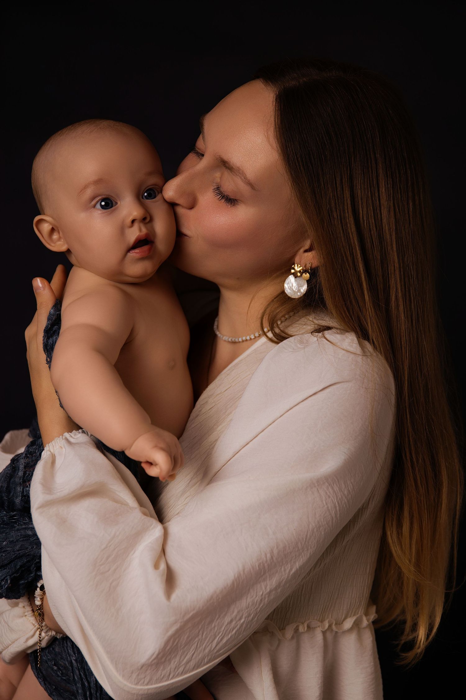 A tender moment captured in a series of photos showing a parent in white embracing and kissing a baby against a dark background.