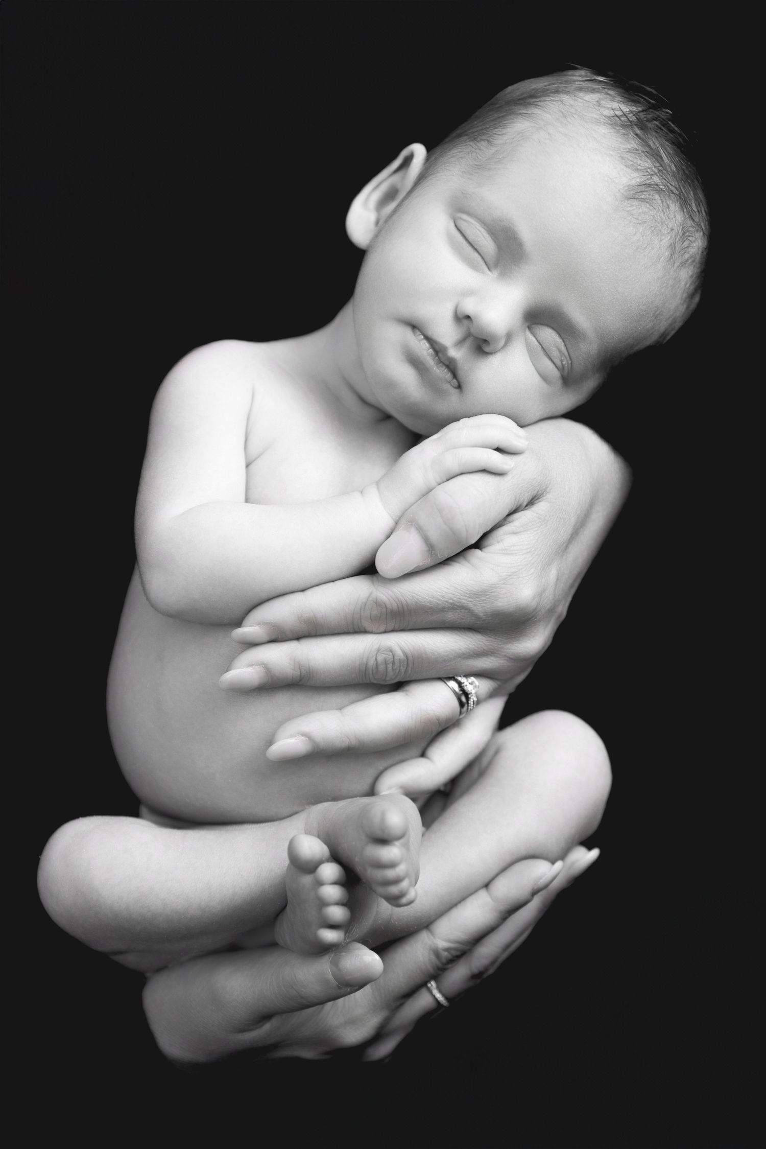 Black and white artistic portraits of a sleeping newborn baby cradled in gentle hands against dark background.
