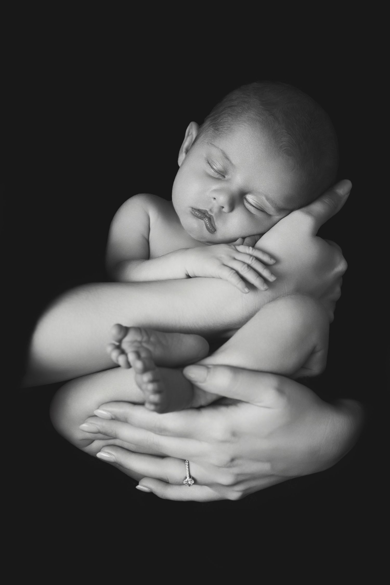 A series of black and white artistic photographs showing a sleeping baby in various curled up poses.