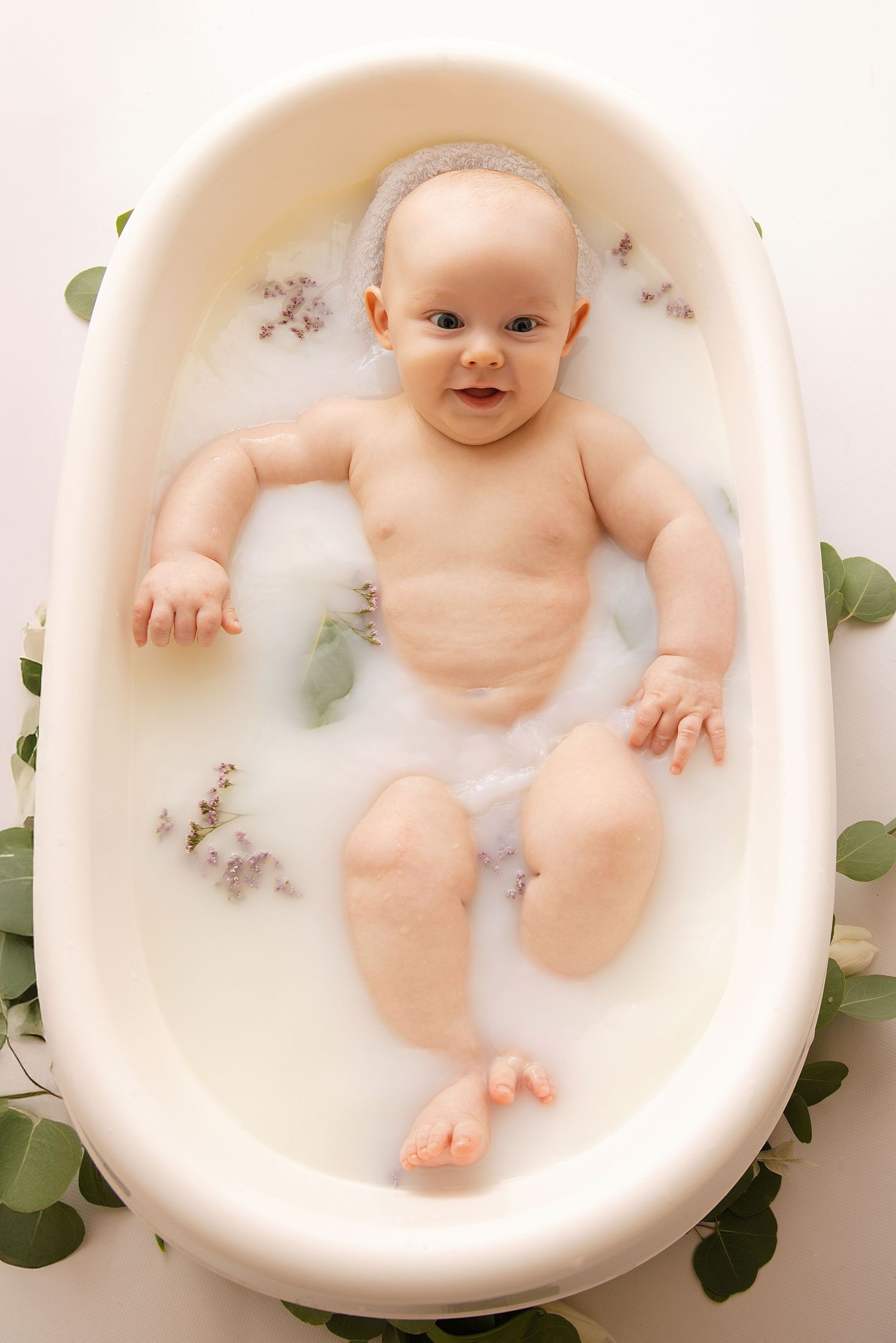 A series of three milk bath photos showing a baby lying in creamy white water with delicate green leaves.