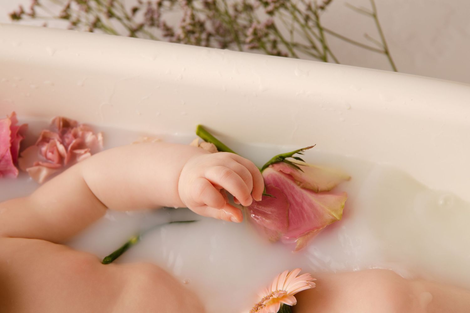 Pink roses and petals float in a white bathtub filled with milky water creating a luxurious spa-like scene.