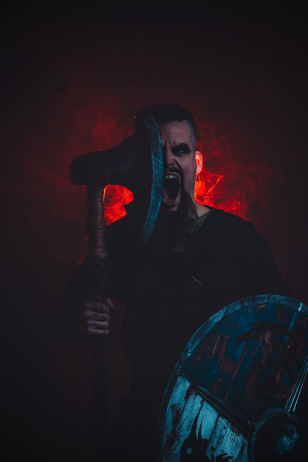 Fierce Viking warrior wielding a battle axe and shield, screaming against a dark red smoky background.